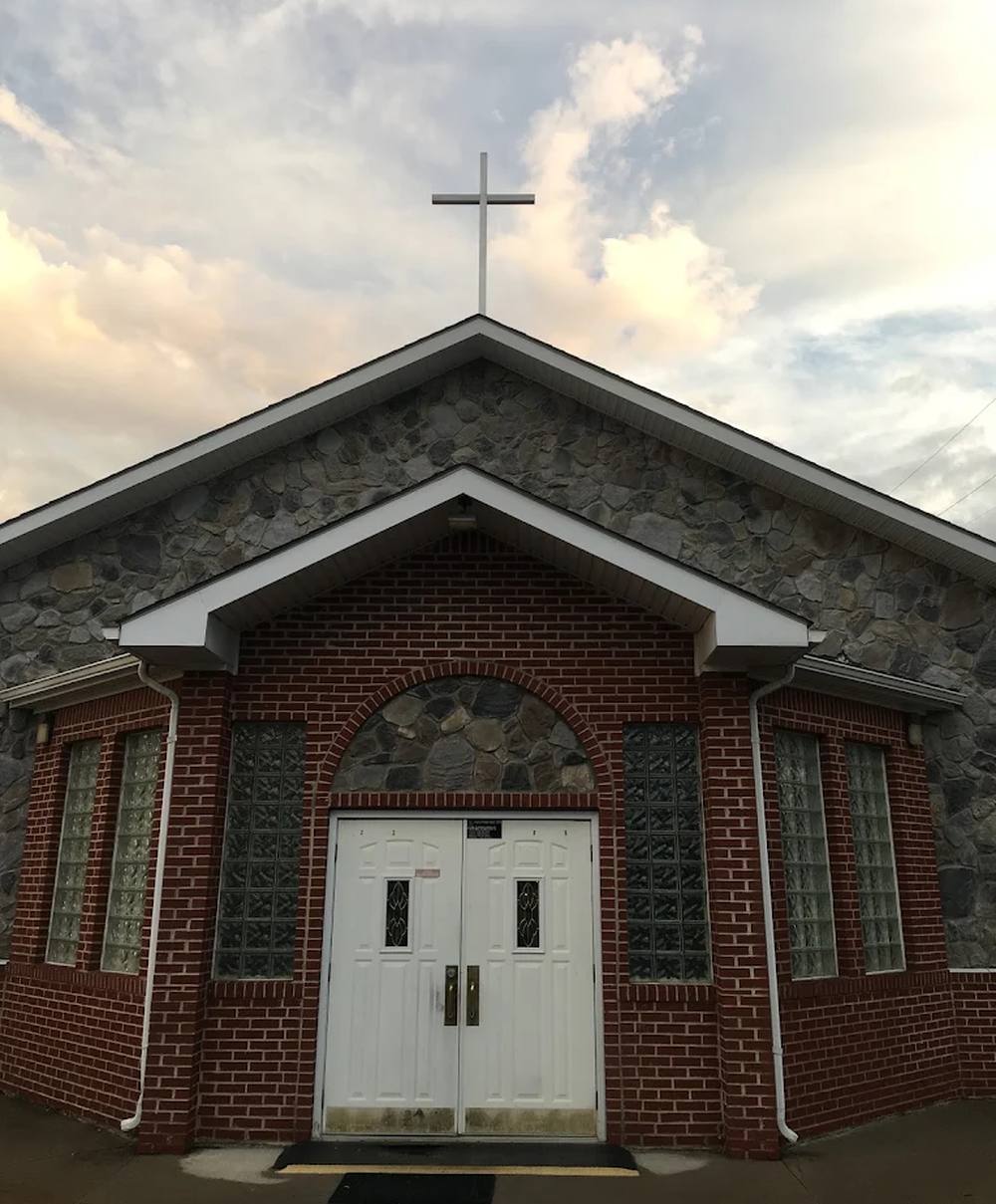 The front entrance of Golgotha Romanian Baptist Church, brick and stone with a cross above the gable